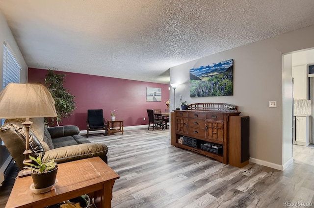 living area with a textured ceiling, light wood-style flooring, and baseboards