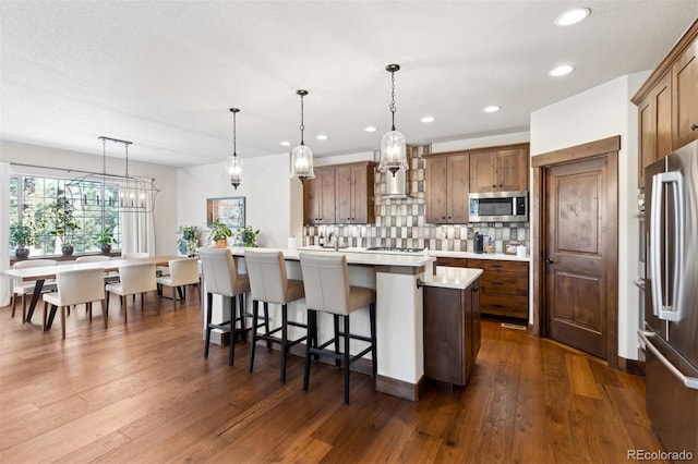 kitchen featuring decorative light fixtures, an island with sink, a breakfast bar area, decorative backsplash, and appliances with stainless steel finishes