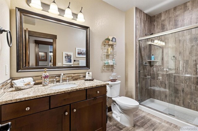 bathroom with wood-type flooring, vanity, a shower with shower door, and toilet