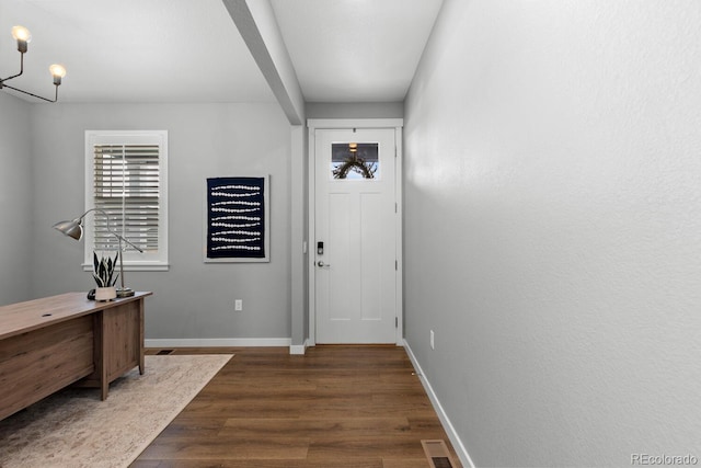 entryway with dark wood-type flooring, visible vents, baseboards, and a chandelier