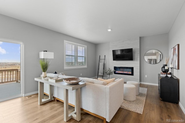 living area featuring visible vents, wood finished floors, baseboards, and a large fireplace