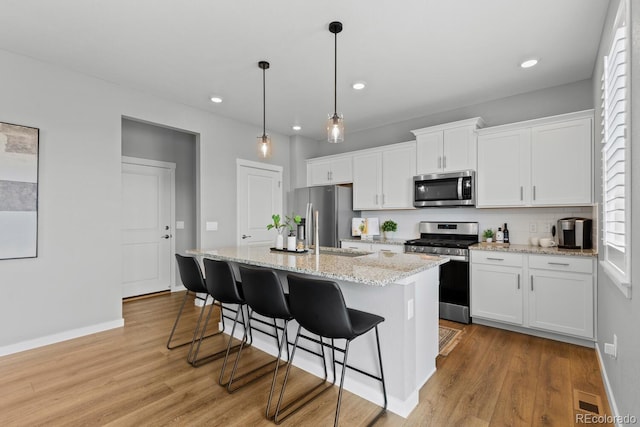 kitchen with a kitchen bar, a kitchen island, stainless steel appliances, white cabinets, and light wood finished floors