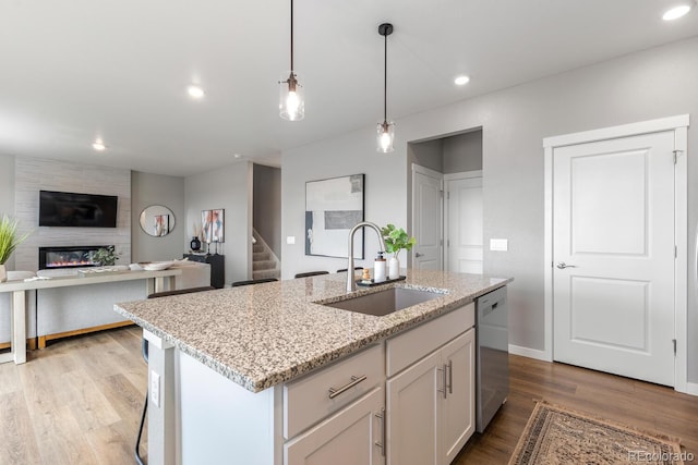 kitchen with light wood finished floors, a sink, recessed lighting, a fireplace, and stainless steel dishwasher