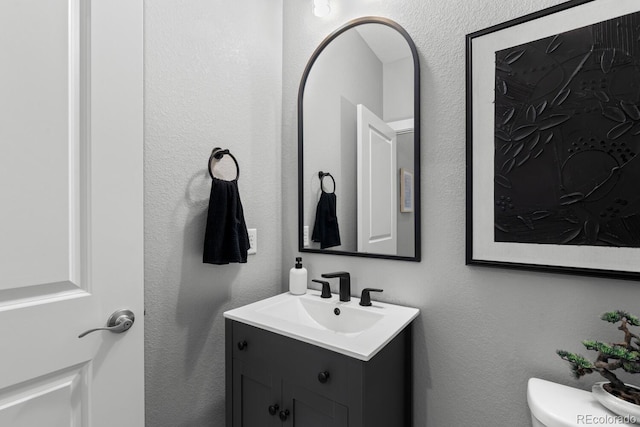 bathroom featuring vanity, toilet, and a textured wall