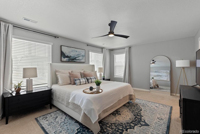 bedroom featuring visible vents, a ceiling fan, a textured ceiling, baseboards, and light colored carpet