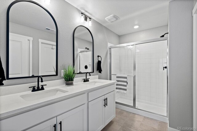 bathroom featuring double vanity, visible vents, a shower stall, and a sink