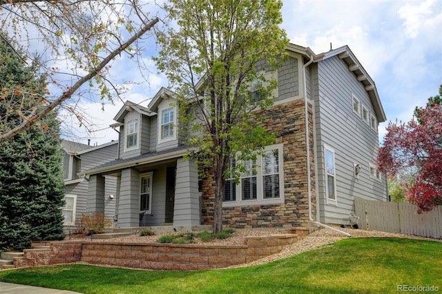 view of front facade with stone siding, a front lawn, and fence