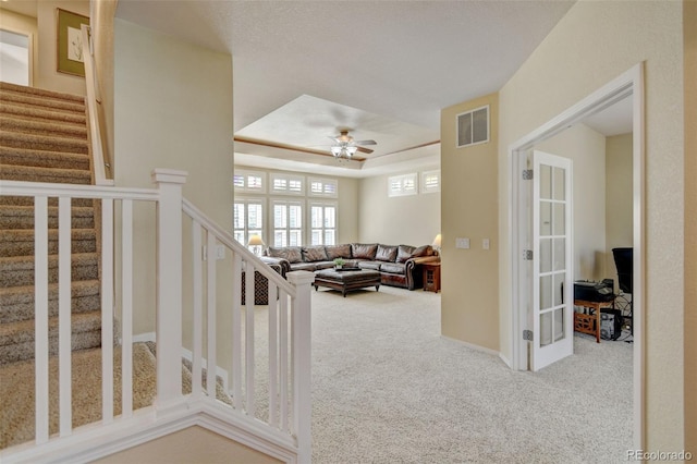 carpeted living room featuring stairway, a raised ceiling, visible vents, a ceiling fan, and baseboards