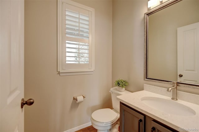 half bath with baseboards, toilet, and vanity