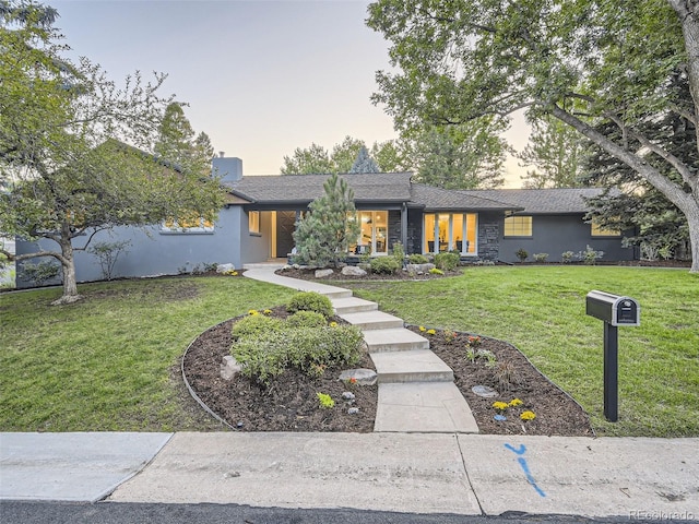 mid-century home featuring a lawn, stucco siding, and roof with shingles