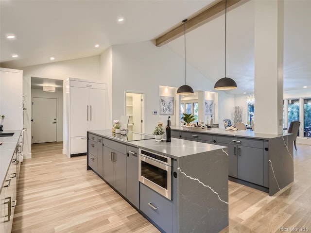 kitchen featuring a center island, gray cabinets, light wood-style flooring, stainless steel microwave, and beamed ceiling