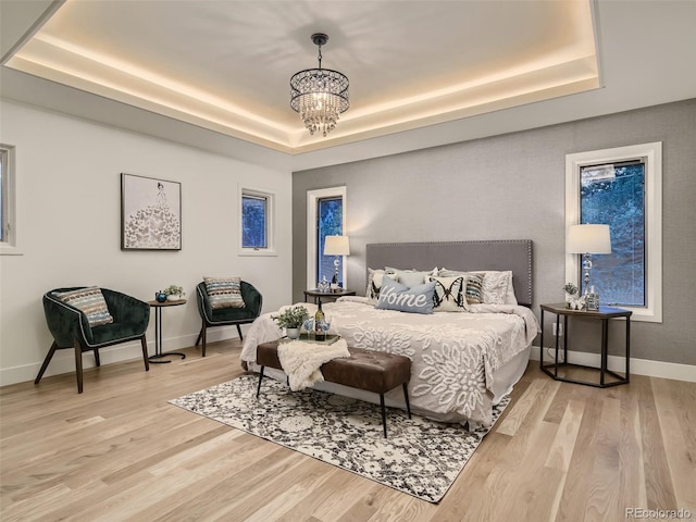 bedroom featuring a tray ceiling, light wood-style flooring, a chandelier, and baseboards