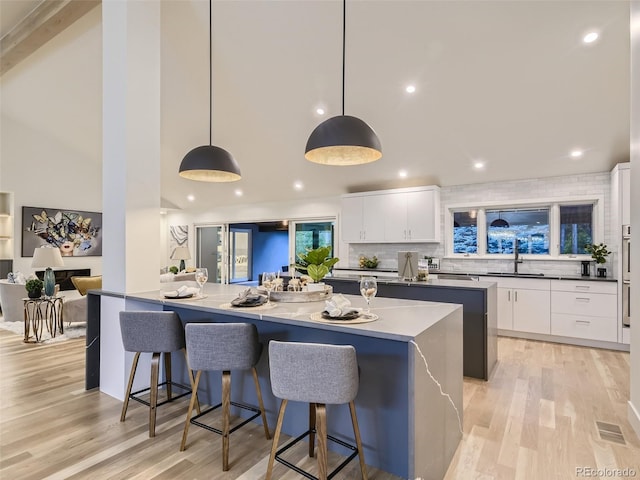 kitchen with a sink, a kitchen island, high vaulted ceiling, white cabinets, and light wood-style flooring