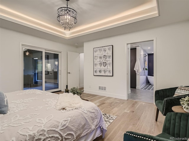 bedroom with a raised ceiling, a chandelier, light wood-type flooring, baseboards, and connected bathroom
