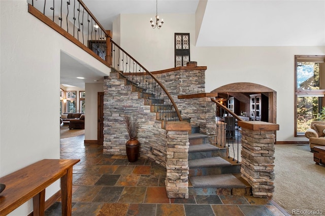 stairway featuring stone finish floor, arched walkways, an inviting chandelier, baseboards, and a towering ceiling