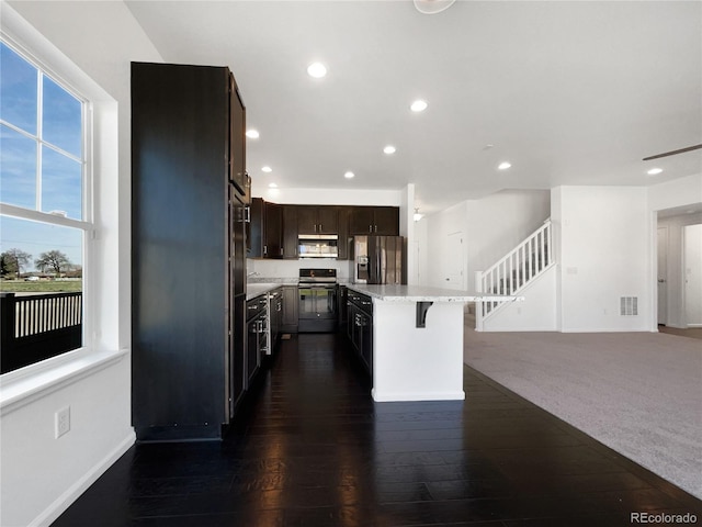 1826 Sunshine Ave, Longmont, CO 80504 - kitchen with appliances with stainless steel finishes, dark brown cabinets, a breakfast bar, recessed lighting, and a kitchen island