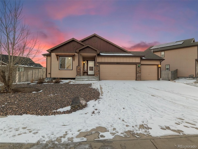 view of front of house featuring a garage, stone siding, fence, and board and batten siding