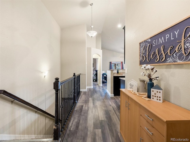 hall featuring lofted ceiling, baseboards, dark wood-style flooring, and an upstairs landing