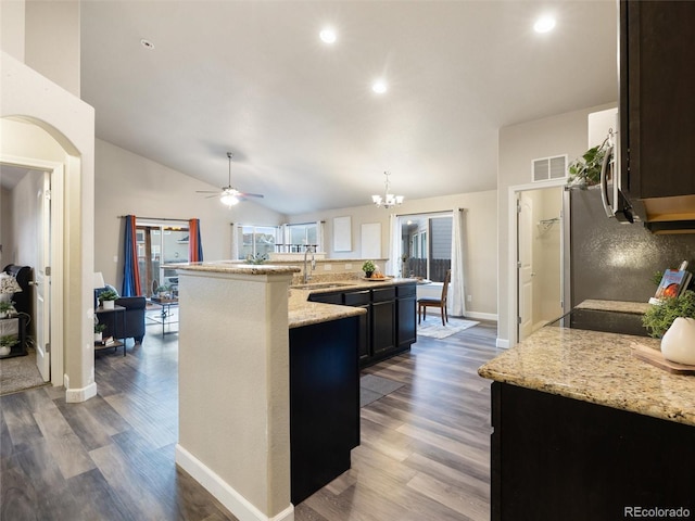 kitchen featuring lofted ceiling, wood finished floors, a sink, visible vents, and light stone countertops