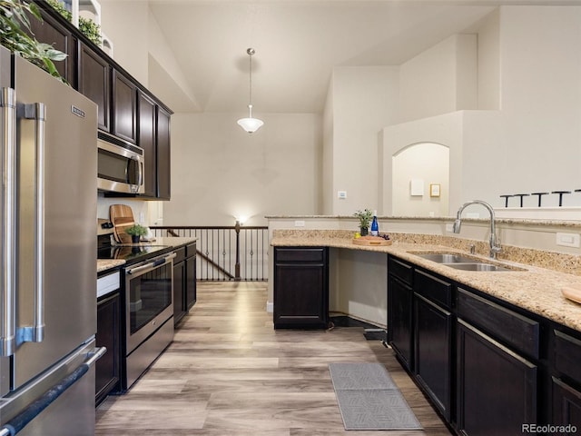 kitchen featuring light stone counters, a sink, appliances with stainless steel finishes, light wood-type flooring, and decorative light fixtures