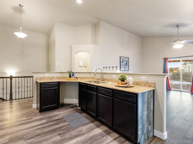 kitchen featuring light stone counters, light wood-style flooring, vaulted ceiling, a sink, and an island with sink