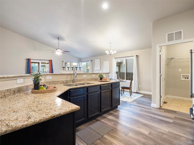 kitchen featuring lofted ceiling, visible vents, light wood-style flooring, a sink, and ceiling fan with notable chandelier