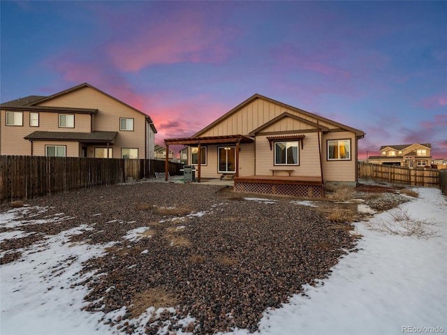 snow covered property featuring a fenced backyard and board and batten siding