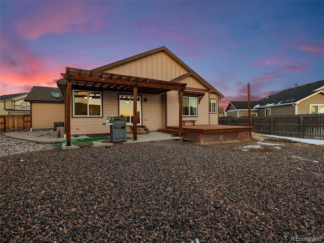 back of house at dusk featuring a patio area, a fenced backyard, board and batten siding, and a wooden deck