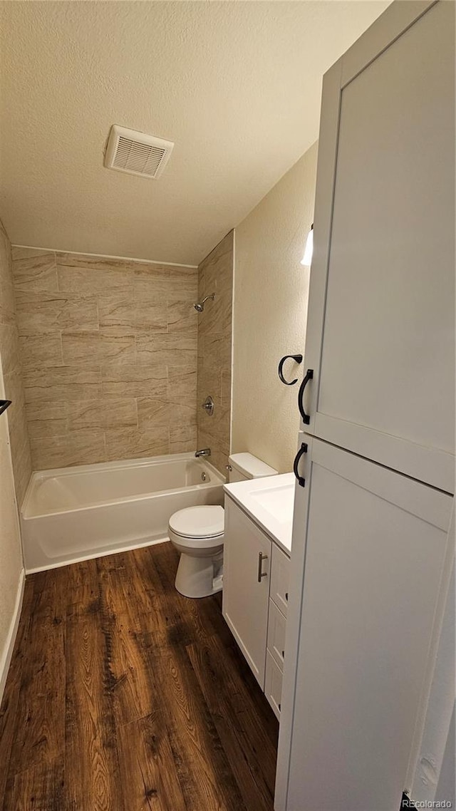 bathroom featuring a textured ceiling, toilet, wood finished floors, visible vents, and  shower combination