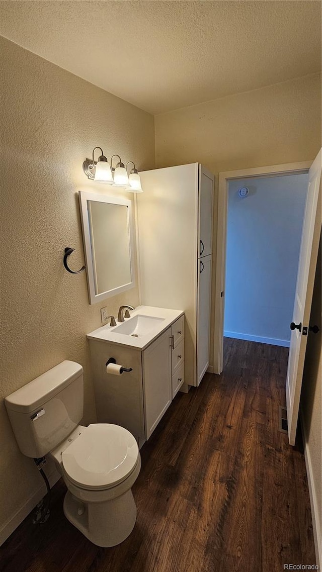 half bath with a textured ceiling, a textured wall, toilet, wood finished floors, and vanity