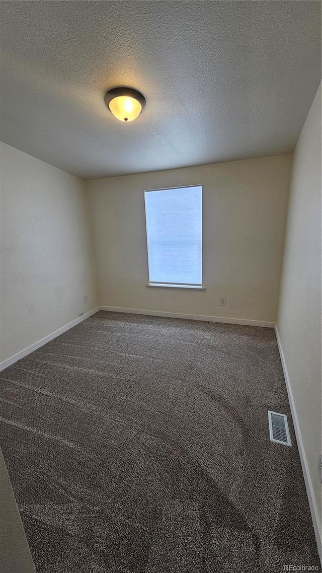 unfurnished room with a textured ceiling, carpet floors, visible vents, and baseboards