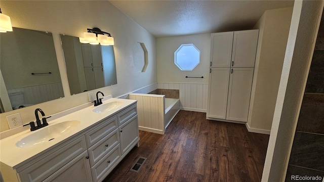 bathroom featuring a wainscoted wall, wood finished floors, a sink, and visible vents