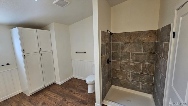 full bathroom with a wainscoted wall, tiled shower, wood finished floors, and visible vents