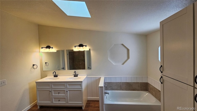 bathroom featuring double vanity, a skylight, a bath, a textured ceiling, and a sink