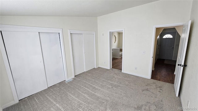 unfurnished bedroom featuring lofted ceiling, baseboards, multiple closets, and carpet flooring