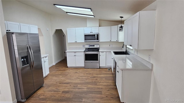 kitchen featuring lofted ceiling, wood finished floors, stainless steel appliances, white cabinetry, and a sink