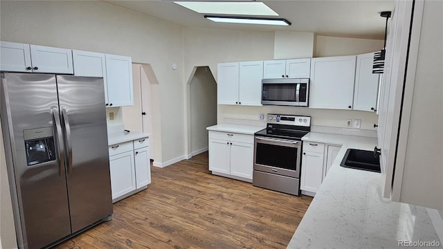 kitchen featuring appliances with stainless steel finishes, white cabinets, vaulted ceiling, a sink, and wood finished floors