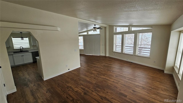 unfurnished living room featuring a wealth of natural light, dark wood finished floors, vaulted ceiling, and a sink