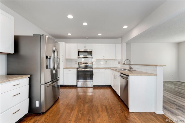 kitchen featuring a sink, stainless steel appliances, a peninsula, decorative backsplash, and dark wood-style flooring