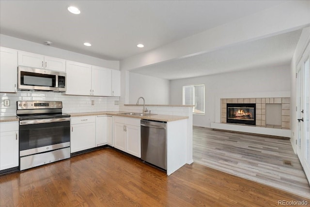 kitchen with light countertops, a peninsula, dark wood-style floors, stainless steel appliances, and a sink