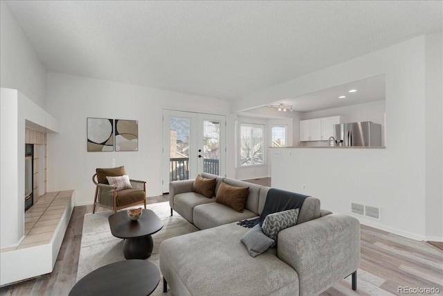 living room with visible vents, light wood-style flooring, french doors, a fireplace, and baseboards