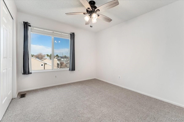 empty room with carpet flooring, a ceiling fan, visible vents, and a textured ceiling