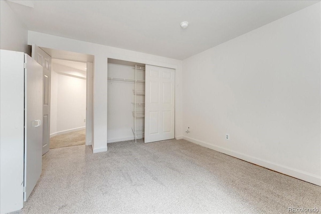 unfurnished bedroom featuring a closet, freestanding refrigerator, and baseboards