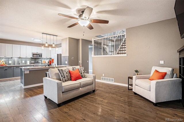 living room with a textured ceiling, ceiling fan, dark wood-type flooring, and visible vents