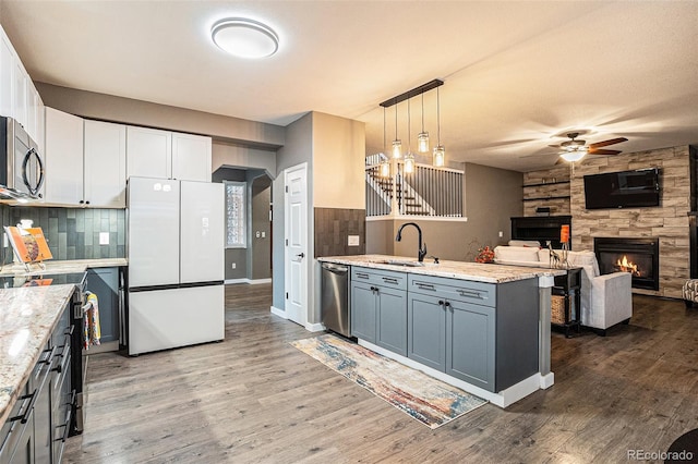 kitchen with a fireplace, stainless steel appliances, ceiling fan, wood finished floors, and a peninsula