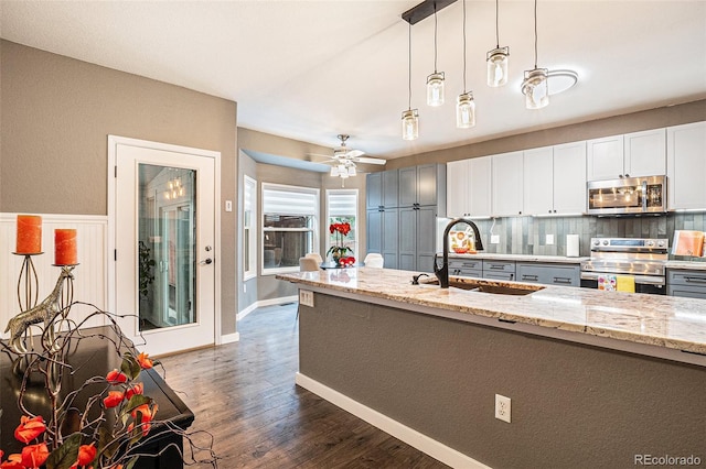 kitchen featuring stainless steel appliances, a sink, backsplash, dark wood-style floors, and decorative light fixtures