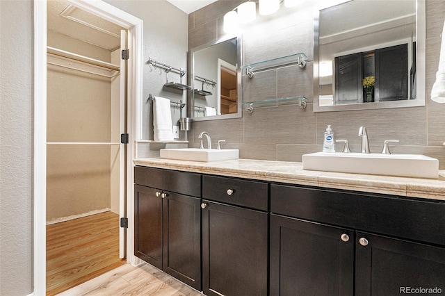 bathroom featuring wood finished floors, double vanity, tasteful backsplash, and a sink