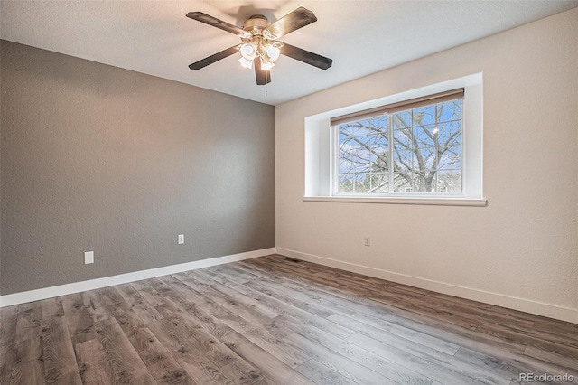 empty room featuring ceiling fan, baseboards, and wood finished floors