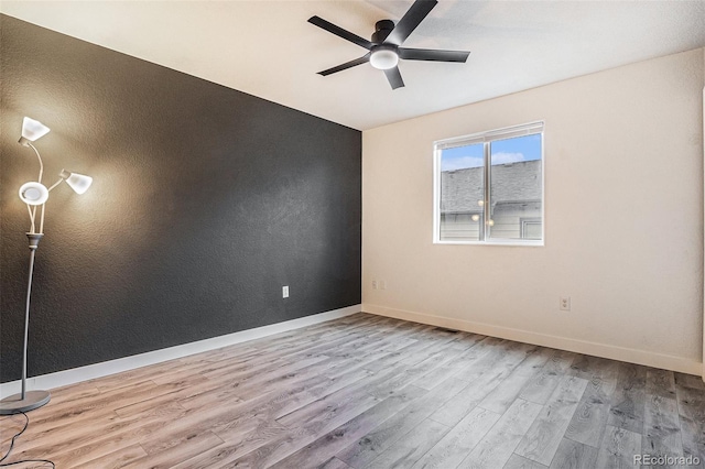 spare room with wood finished floors, a ceiling fan, and baseboards