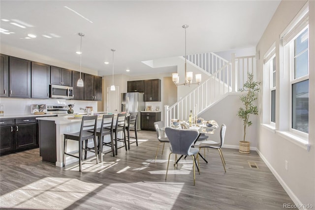 kitchen featuring appliances with stainless steel finishes, decorative light fixtures, a kitchen bar, dark brown cabinets, and a center island with sink